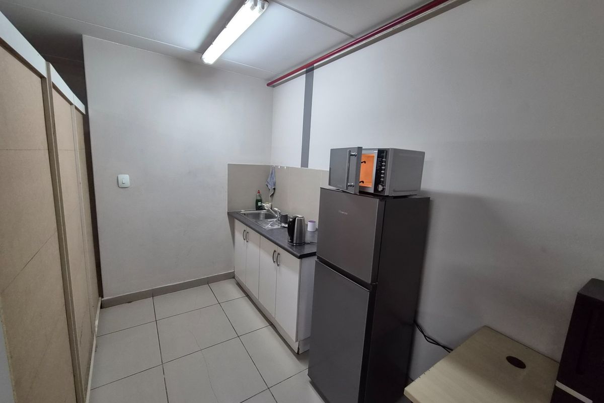 A functional kitchenette area featuring built-in cabinetry, a stainless steel sink, and tiled flooring, suitable for office or industrial utility use.