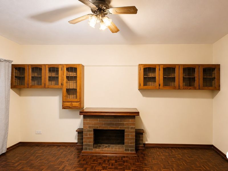A living room featuring a brick fireplace with a wooden mantel, built-in wall cabinetry, a ceiling fan, and classic parquet flooring.