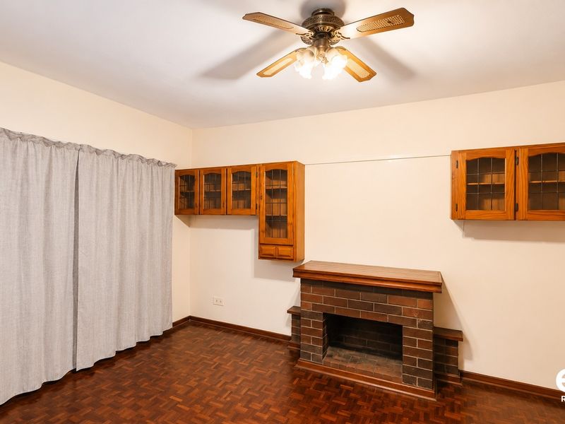 Living room featuring a brick fireplace, built-in wooden cabinetry, ceiling fan, and parquet flooring.
