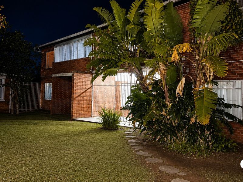 Night view of the rear brick apartment facade featuring a lawn, security gates, and a stone pathway.