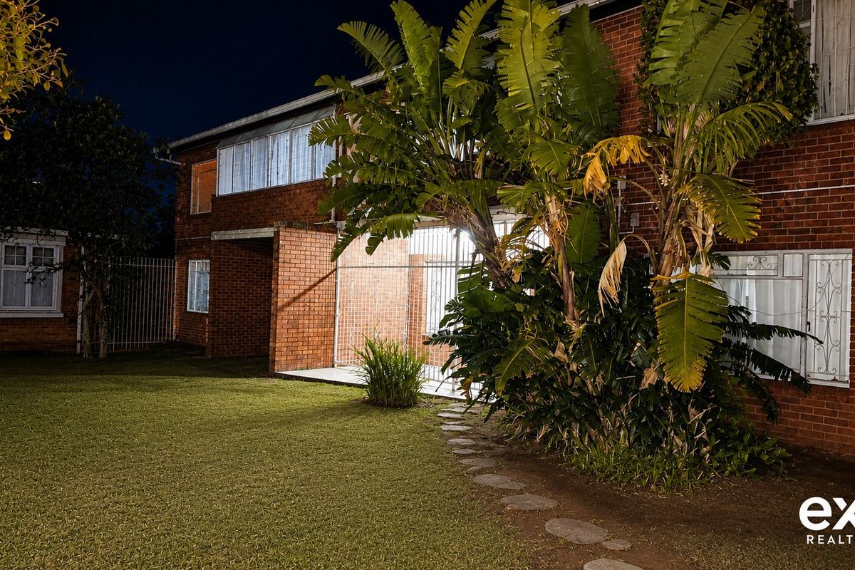 Night view of the rear brick apartment facade featuring a lawn, security gates, and a stone pathway.