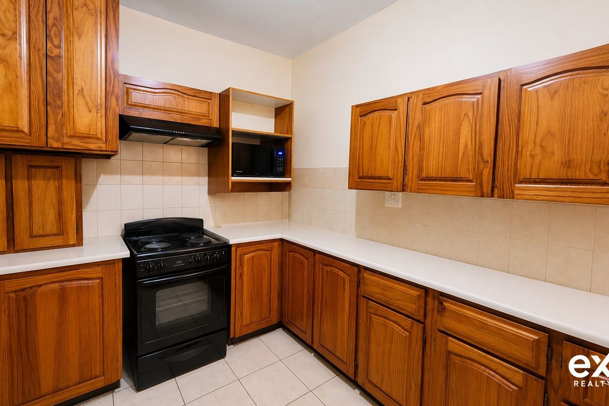 A functional kitchen featuring wooden cabinetry, laminate countertops, a freestanding stove with extractor fan, and tiled finishes throughout.