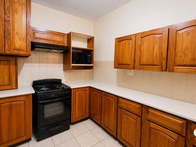 A functional kitchen featuring wooden cabinetry, laminate countertops, a freestanding stove with extractor fan, and tiled finishes throughout.