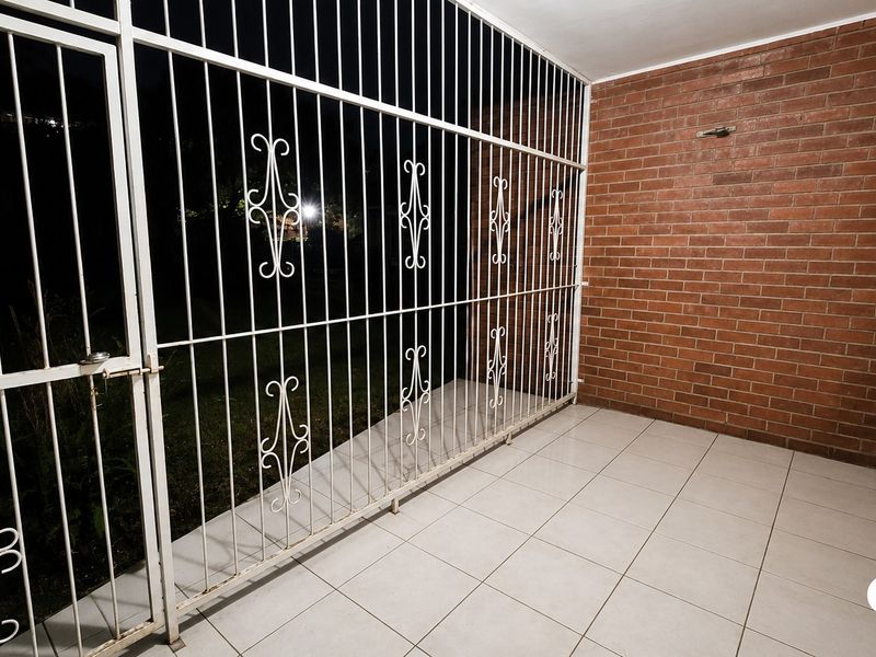 A covered patio area featuring tiled flooring, an exposed brick wall, and a secure metal gate enclosure.
