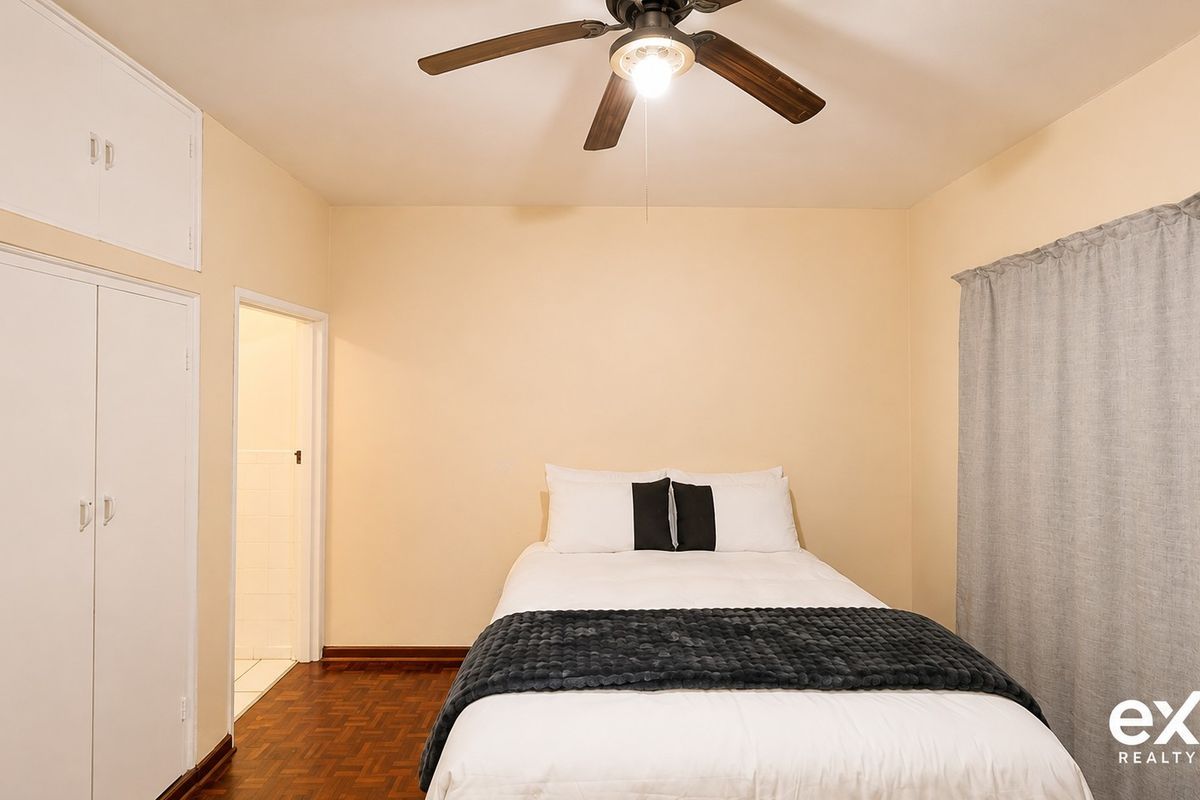 A bedroom featuring parquet flooring, built-in cupboards with overhead storage, and a ceiling fan.