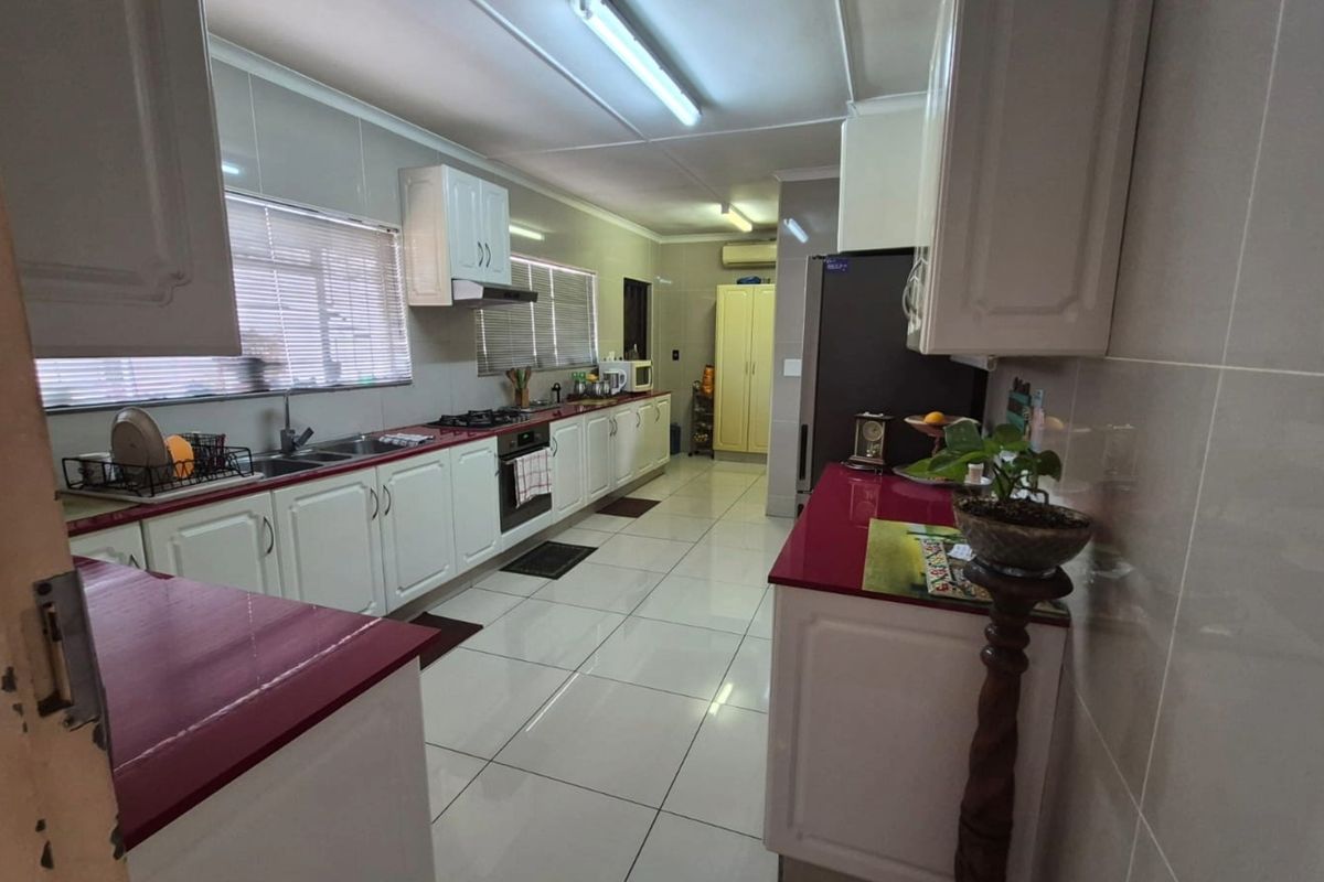 A functional kitchen featuring white cabinetry, contrasting red countertops, tiled walls, and integrated appliances including a gas hob and oven.