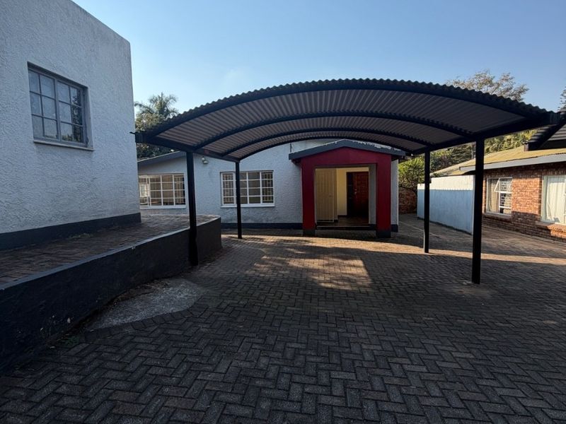 Front exterior view of the property featuring a large covered carport and paved driveway area leading to the main entrance.