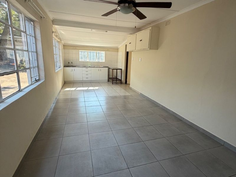 A functional, empty kitchen space featuring tiled flooring, built-in cabinetry, a tiled backsplash, and a ceiling fan.