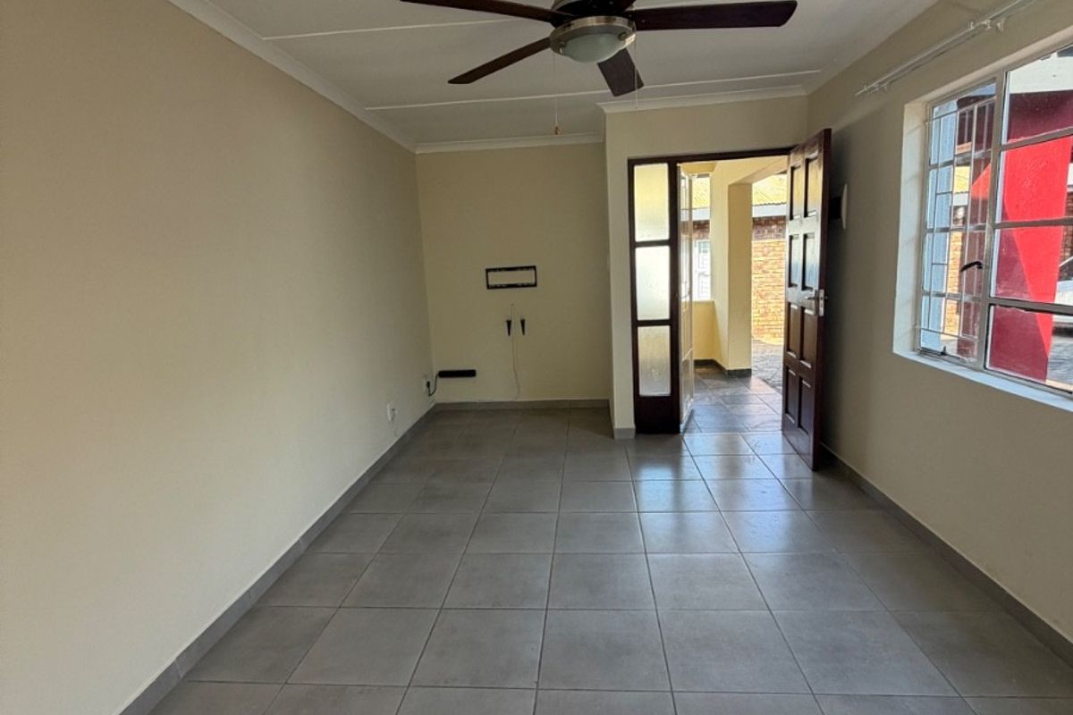 An empty living room featuring neutral tiled flooring, a ceiling fan, and direct access to an outdoor area through a timber door.