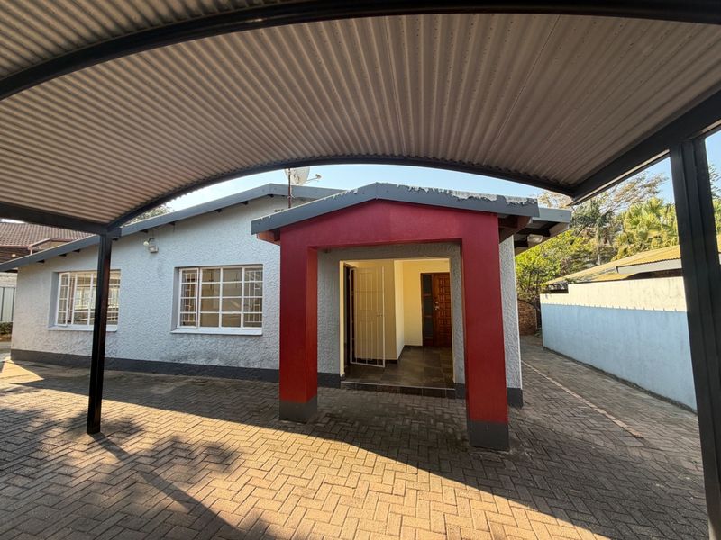 Front exterior view featuring a covered carport, paved driveway, and a distinct red-accented entrance with a secure gate and timber door.