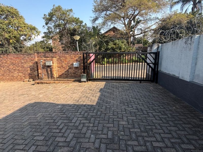 A secure front entrance featuring a paved brick driveway, metal gate, and perimeter boundary wall topped with security razor wire.