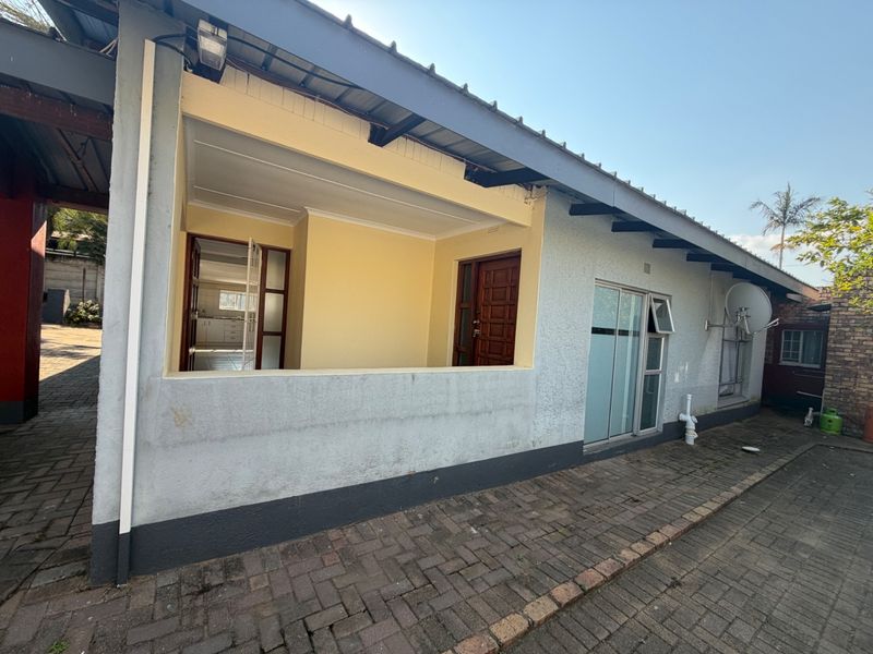 Rear exterior view of the property featuring a covered patio area, paved driveway, and sliding glass door access to the interior.