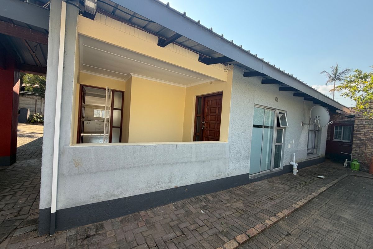 Rear exterior view of the property featuring a covered patio area, paved driveway, and sliding glass door access to the interior.