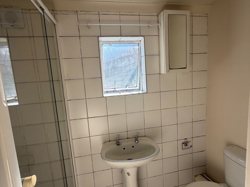 A functional bathroom featuring a pedestal sink, toilet, and shower enclosure with tiled walls and flooring, currently in need of cosmetic updates.