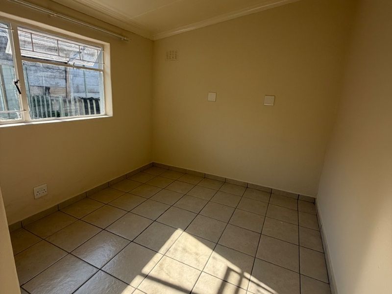 A clean, empty bedroom featuring neutral tiled flooring and natural light from a side window, providing a versatile space ready for customization.