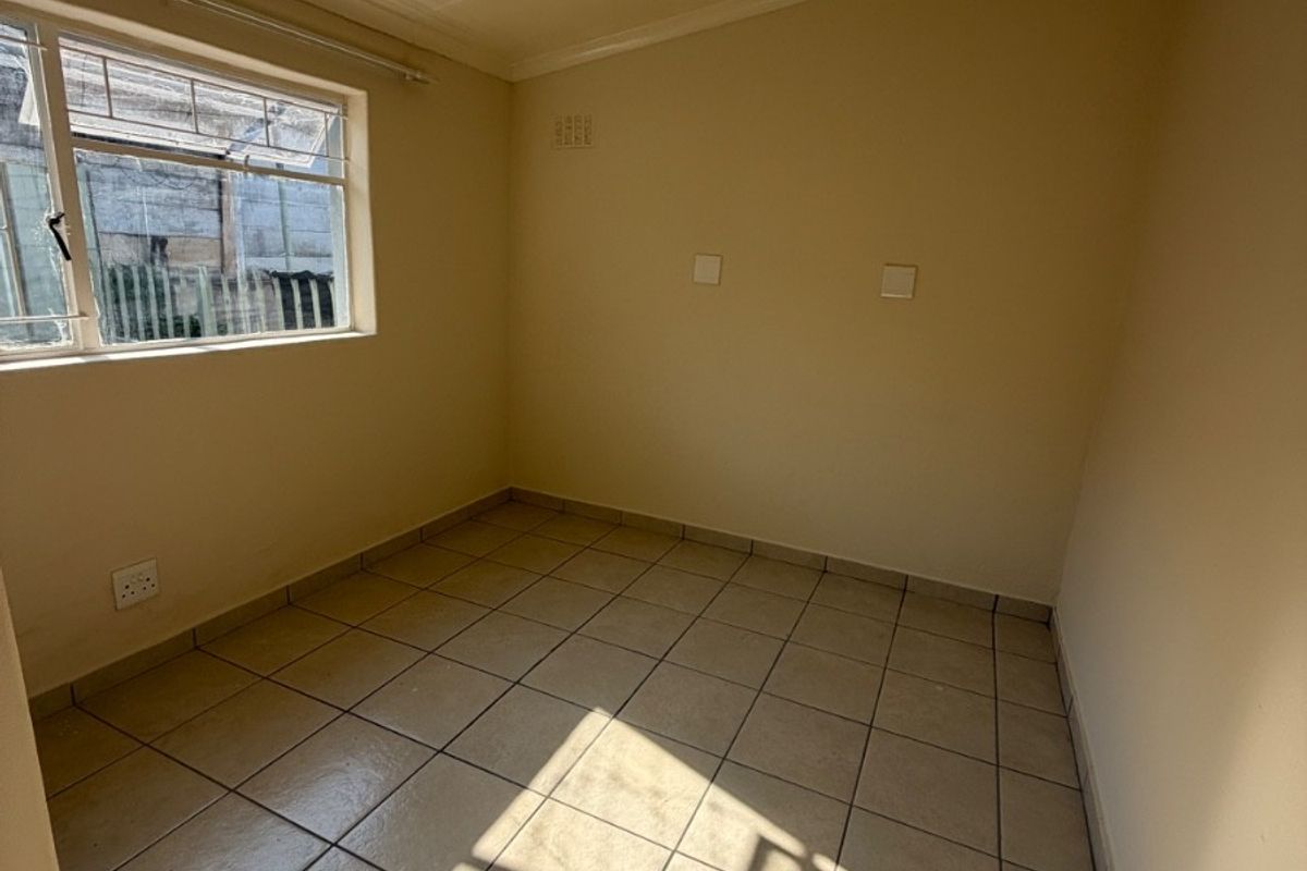 A clean, empty bedroom featuring neutral tiled flooring and natural light from a side window, providing a versatile space ready for customization.