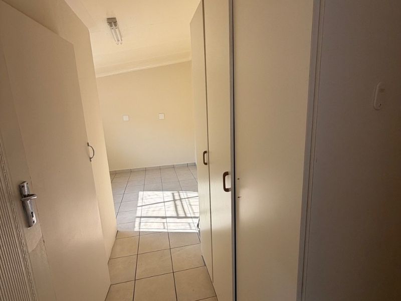 A functional hallway featuring tiled flooring and built-in storage cupboards, leading into an adjacent room.