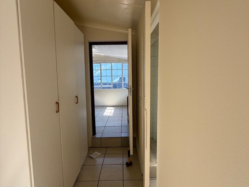 A functional hallway featuring built-in storage cupboards and tiled flooring, providing access to adjacent rooms and an exterior area.