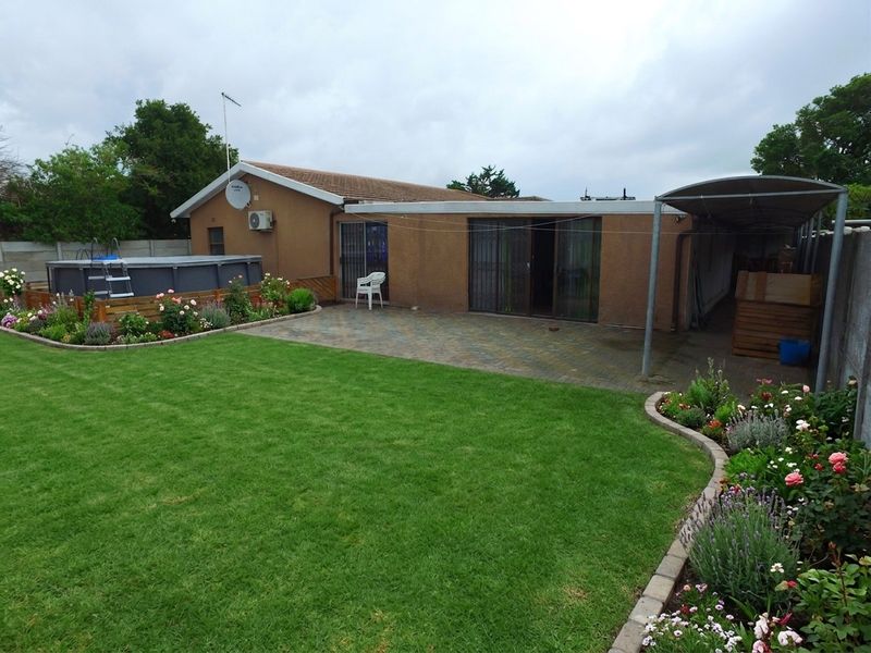 Rear view of the property featuring a paved patio, landscaped garden, above-ground pool, and a covered carport area.