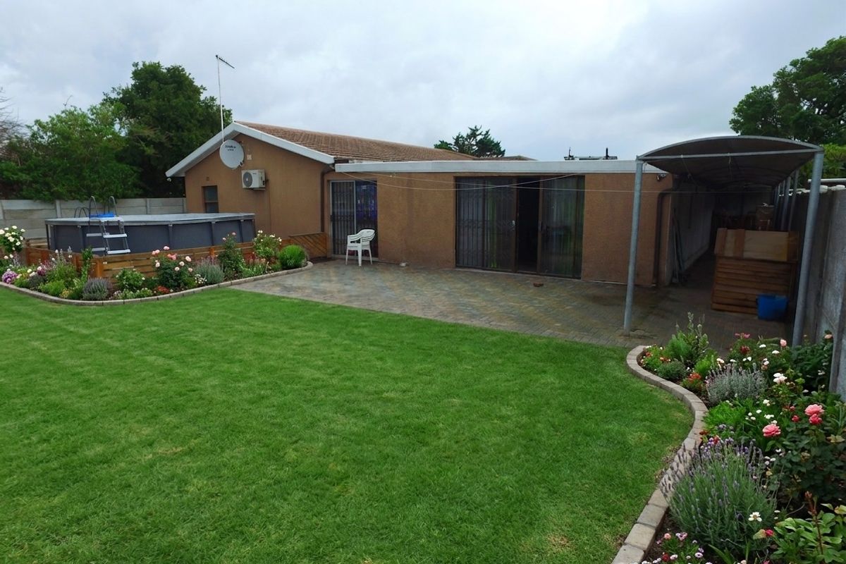Rear view of the property featuring a paved patio, landscaped garden, above-ground pool, and a covered carport area.