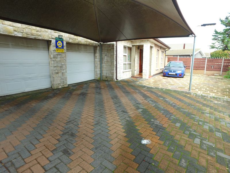Front exterior view featuring a double garage, stone-clad facade, and a paved driveway with a shade sail structure.