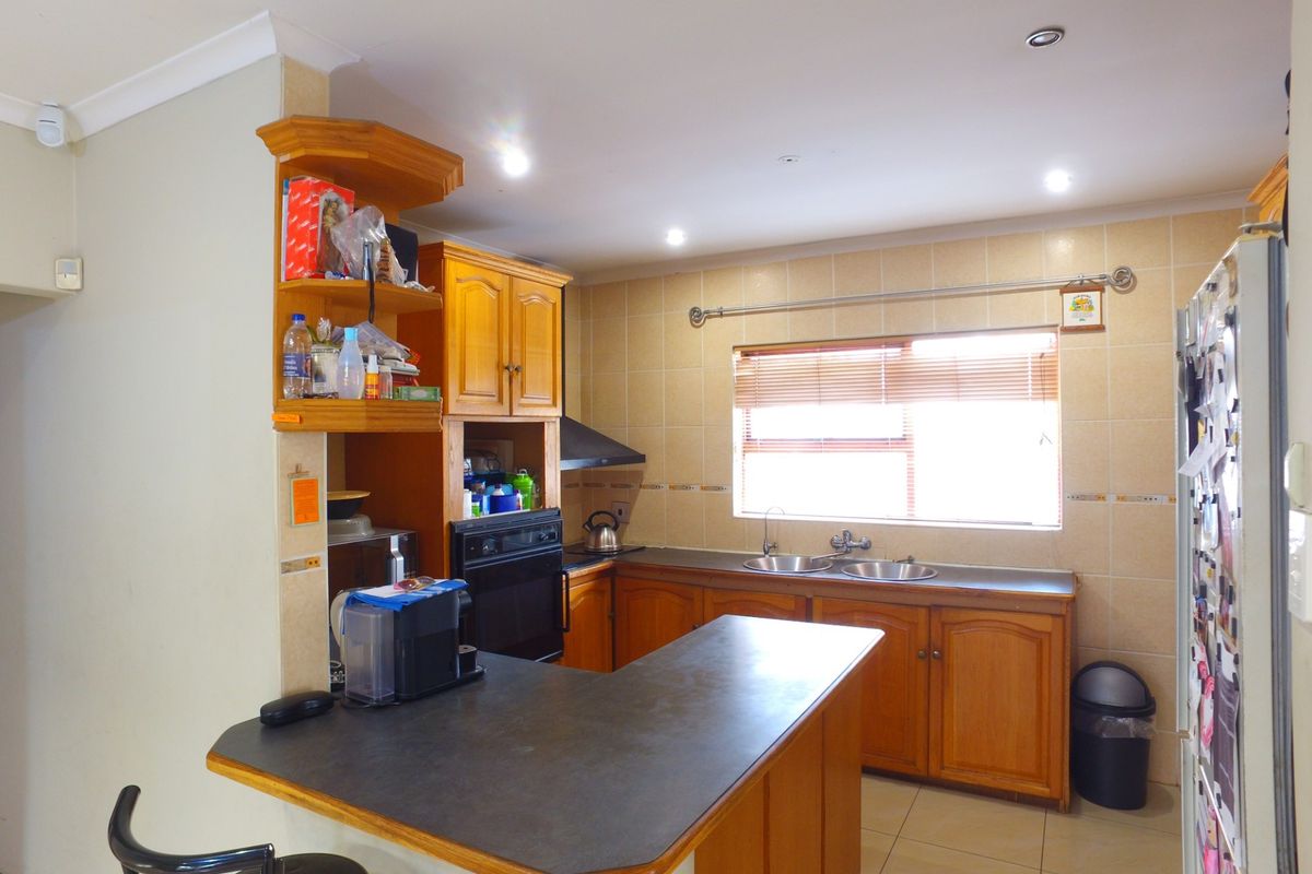 A functional kitchen featuring wooden cabinetry, laminate countertops, a double basin sink, built-in oven, and a breakfast bar with tiled flooring.