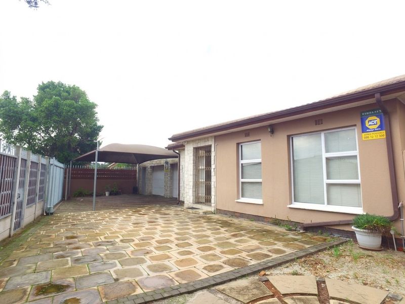 Front exterior view of the property featuring a paved driveway, shade sail structure, and secure perimeter fencing.