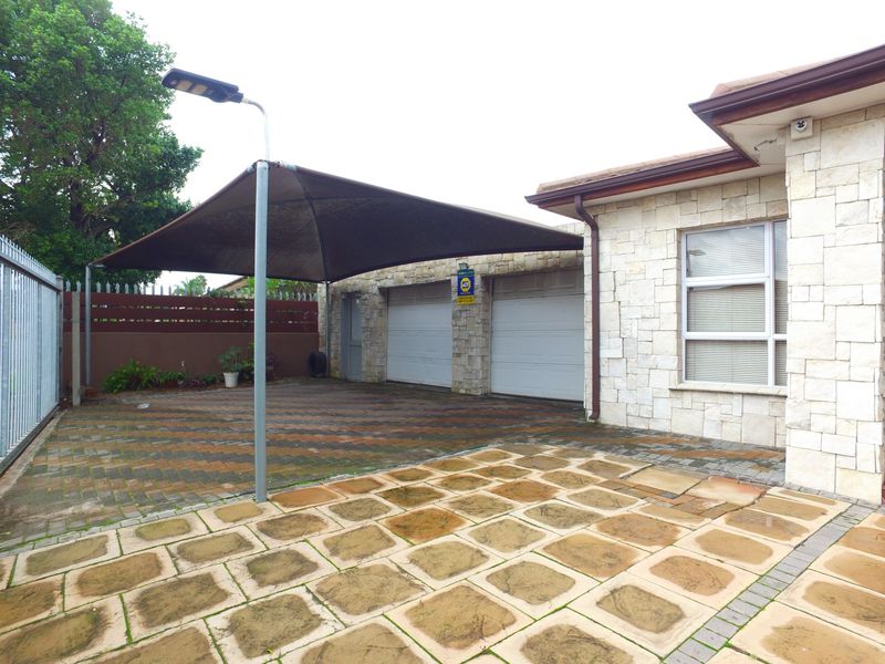 Front exterior view featuring a double garage with stone cladding, a paved driveway, and a shade sail structure for covered parking.