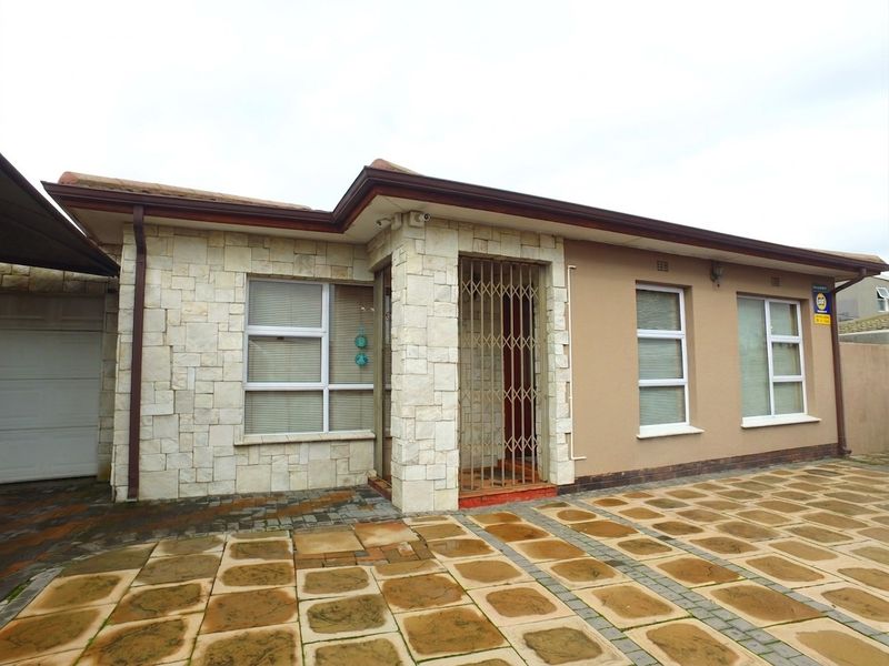 Front facade of the house featuring stone cladding, paved driveway, and secure entrance with a metal security gate.