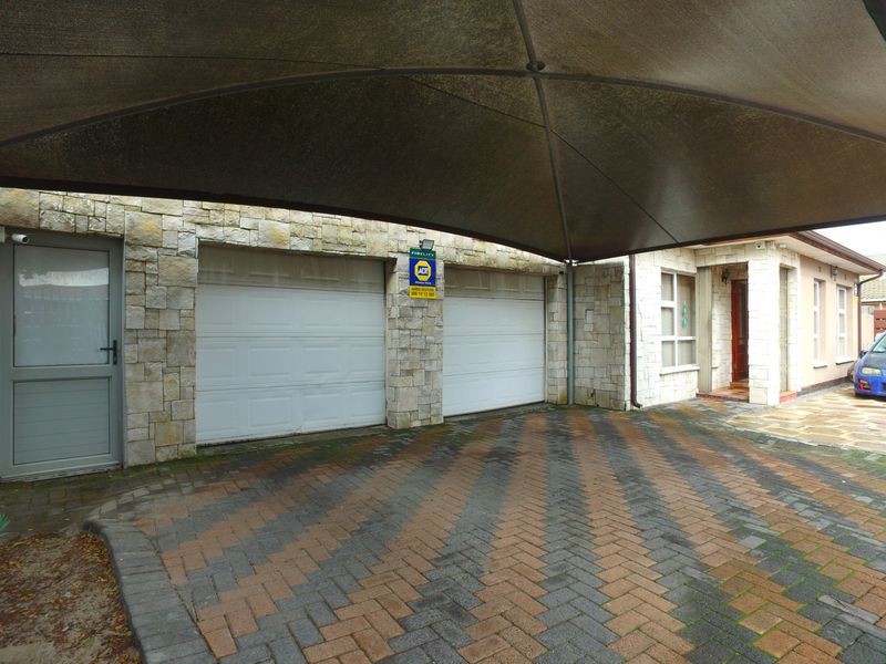 Front exterior view featuring a double garage with stone cladding, a paved driveway, and a large overhead shade sail.