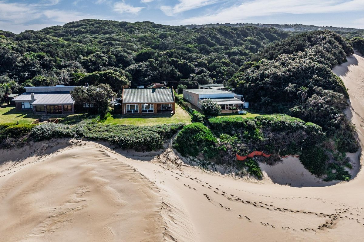 Aerial view of coastal residential properties situated directly adjacent to large sand dunes and dense indigenous forest.