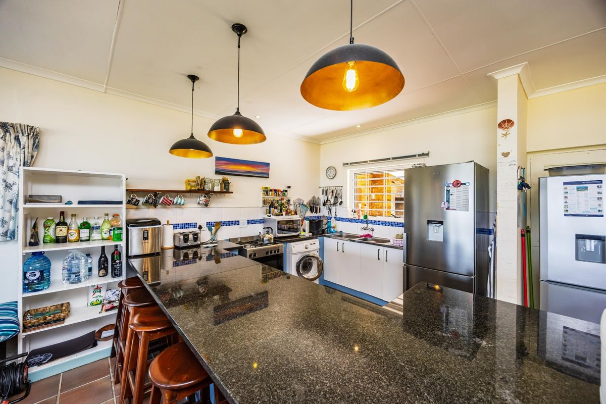 Functional kitchen featuring a large granite breakfast bar, built-in cabinetry, stainless steel sink, and integrated hob and oven.