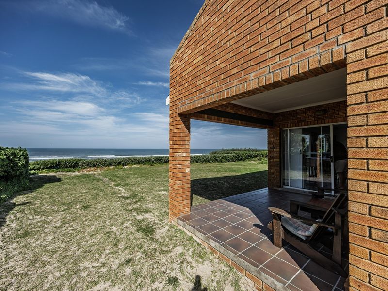 A covered brick patio featuring tiled flooring and sliding glass doors, offering direct access to the garden and scenic ocean views.