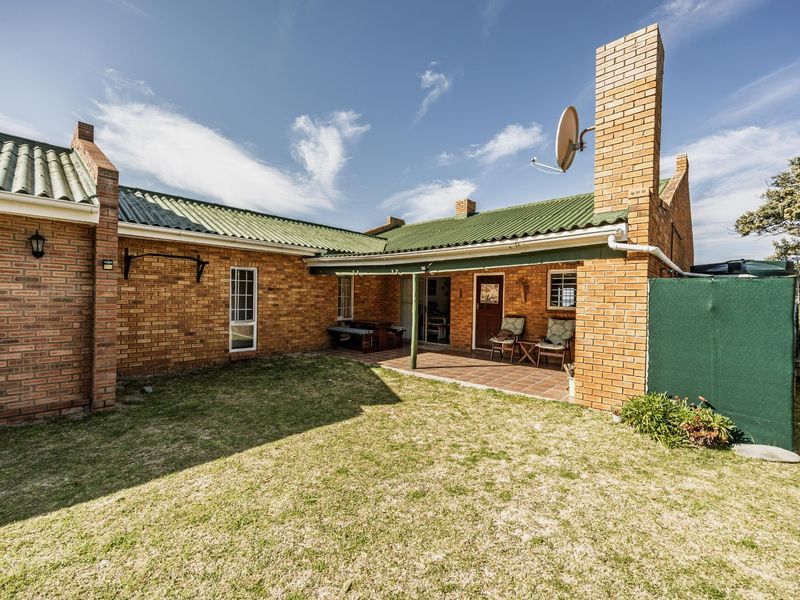 Rear view of the property featuring a face-brick facade, green corrugated metal roof, and a covered patio area overlooking the garden.