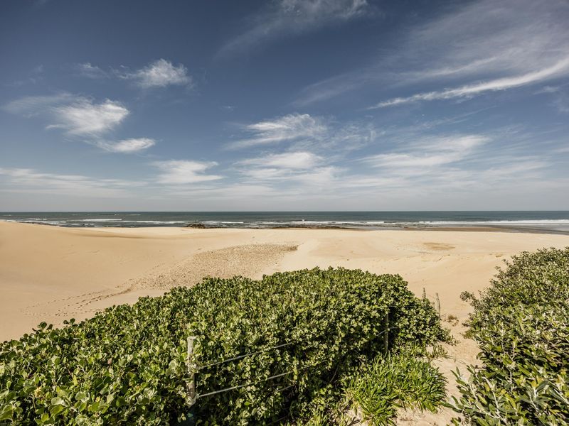 A scenic view of the coastline featuring expansive sand dunes and the ocean under a clear blue sky.