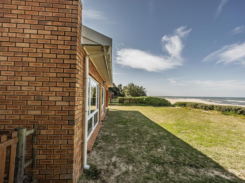 Rear view of the property featuring a brick exterior, lawn area, and direct access to the beach and ocean.