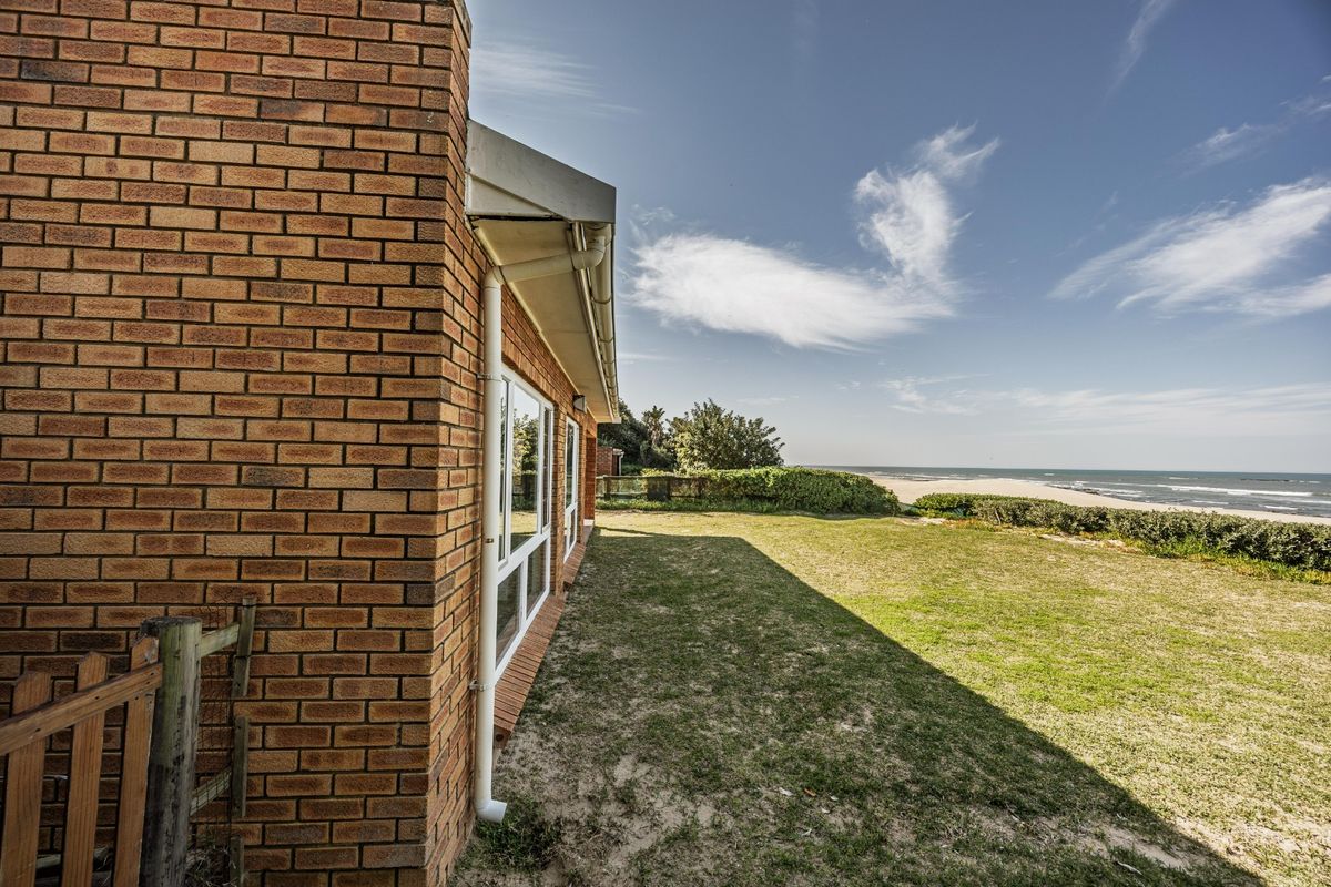 Rear view of the property featuring a brick exterior, lawn area, and direct access to the beach and ocean.