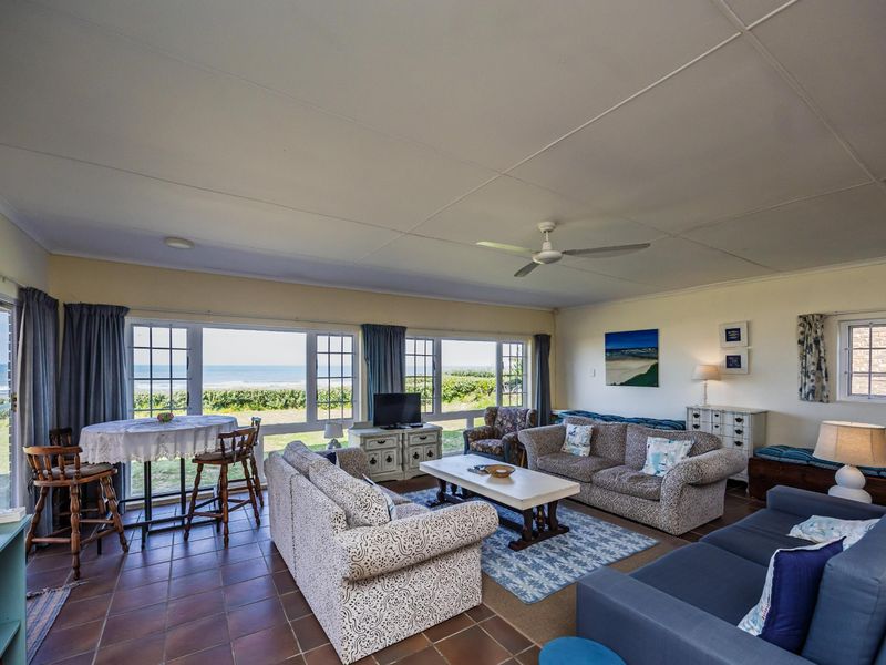 Spacious living area featuring tiled flooring, a ceiling fan, and large windows offering expansive ocean views and natural light.