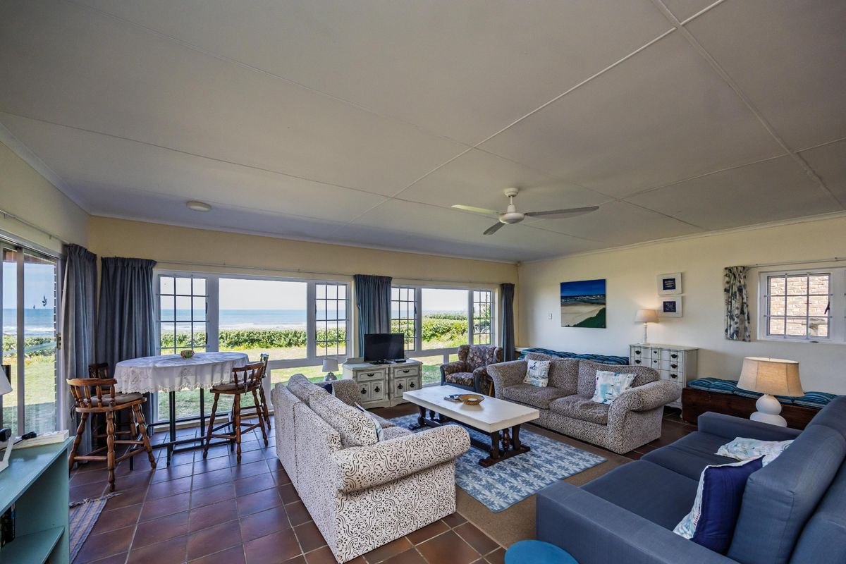 Spacious living area featuring tiled flooring, a ceiling fan, and large windows offering expansive ocean views and natural light.