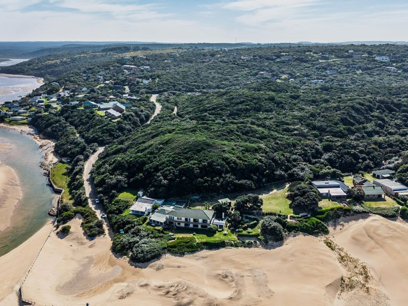 An aerial view of a coastal property situated along an estuary, surrounded by natural dunes and dense coastal vegetation.