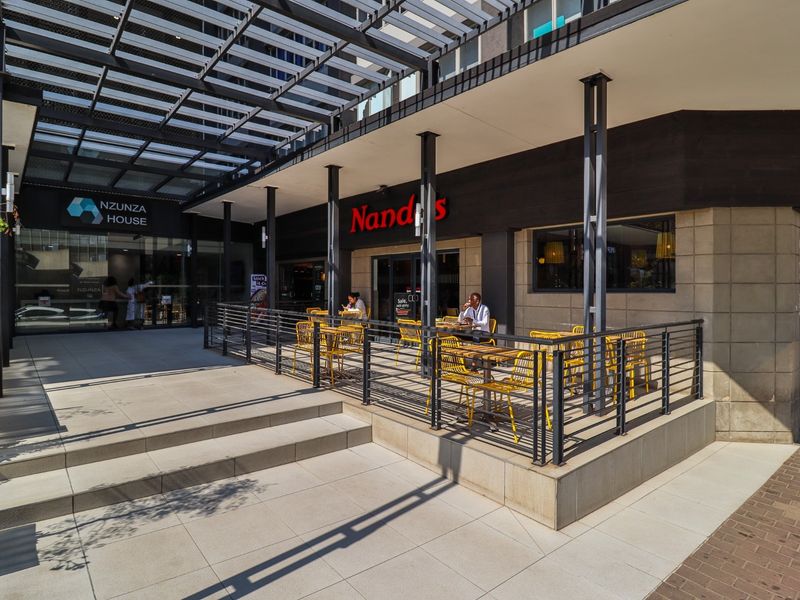 A modern commercial outdoor seating area featuring a metal pergola, steel structural columns, and tiled flooring, providing a well-maintained exterior space for patrons.
