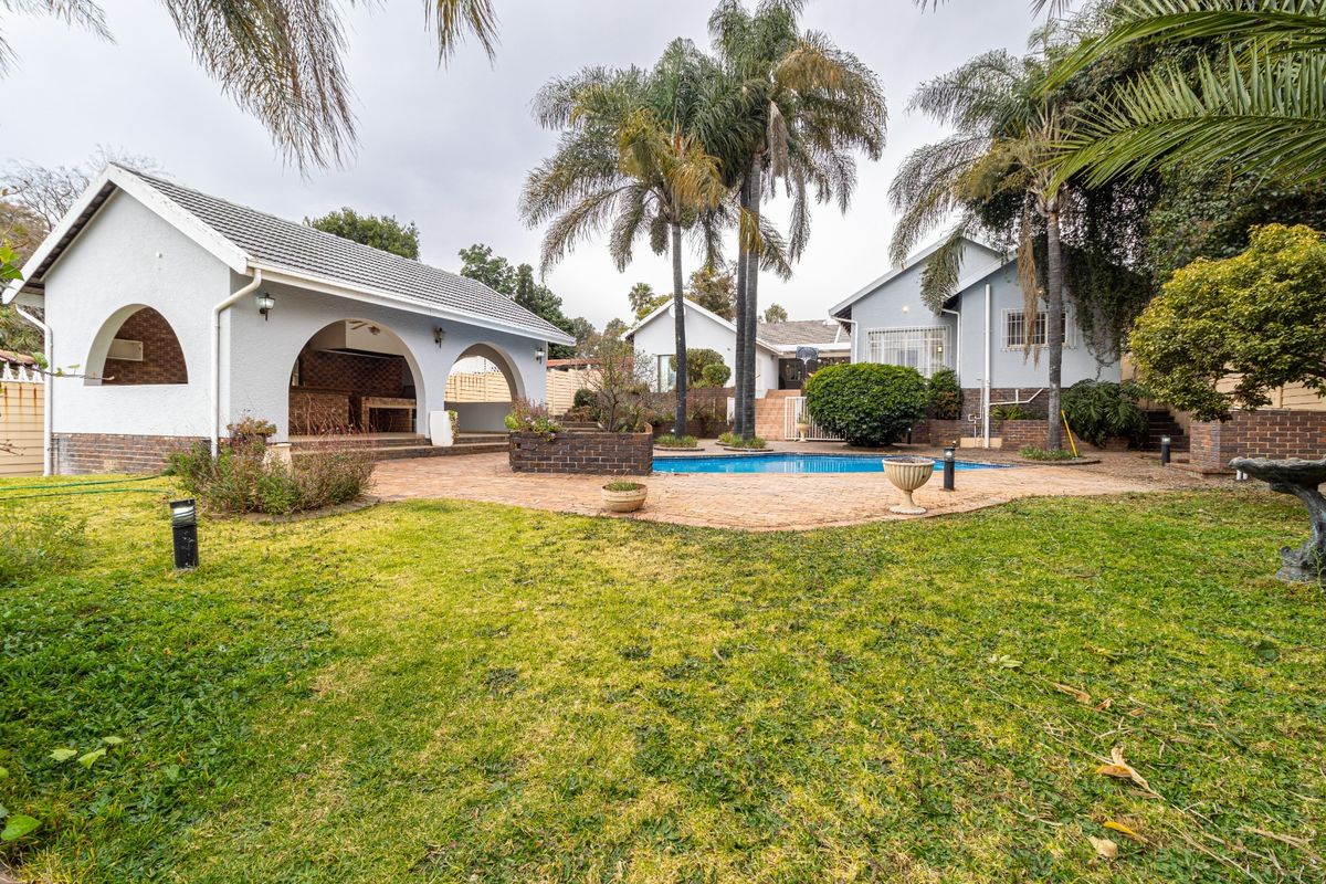 Spacious rear garden featuring a swimming pool, brick-paved patio area, and a covered outdoor entertainment space with arched architectural details.