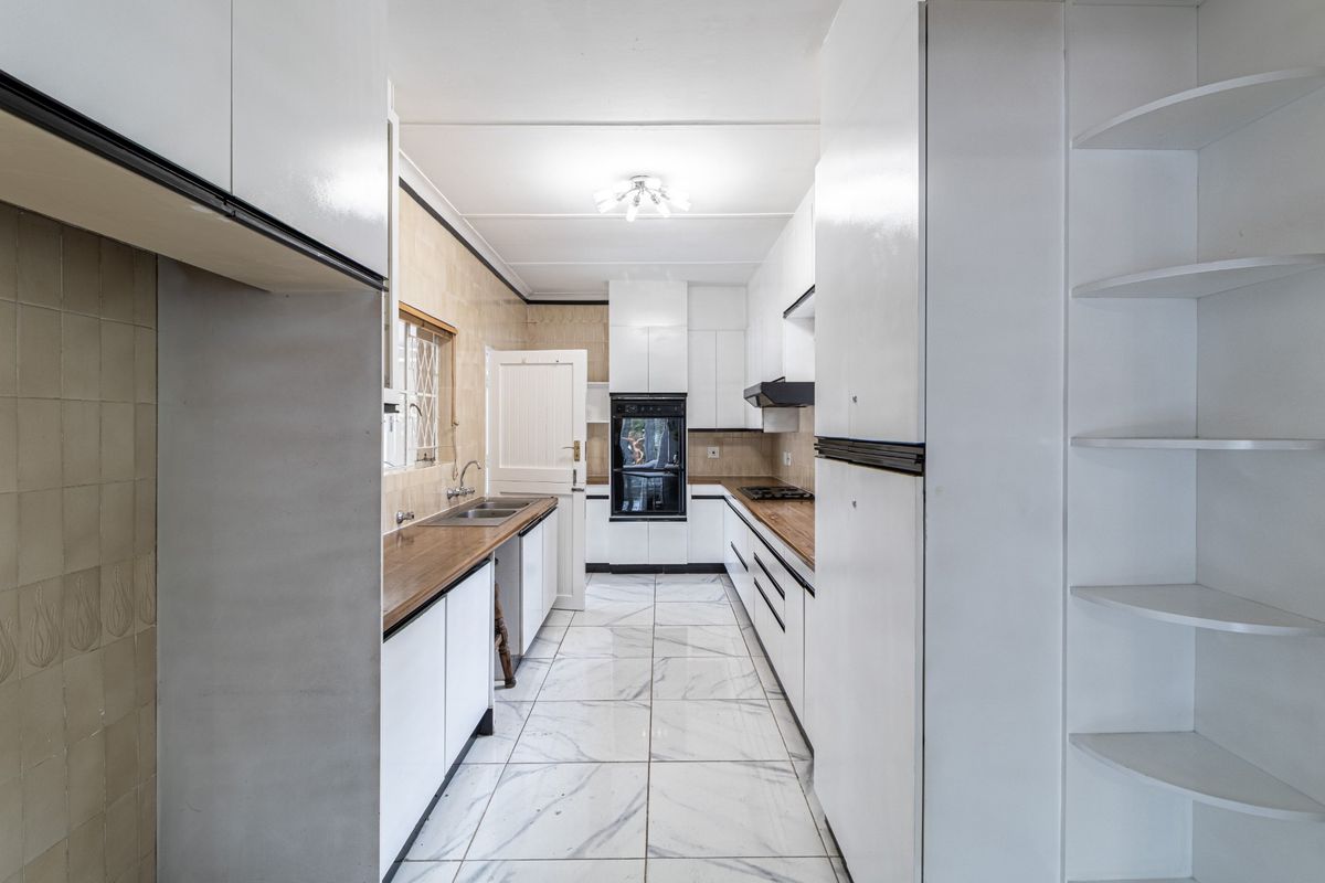A galley-style kitchen featuring white cabinetry, wood-look countertops, a built-in oven, hob, extractor fan, and marble-look tiled flooring.