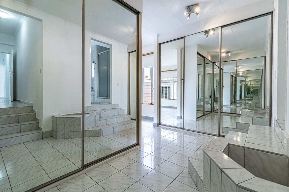 Spacious bedroom featuring extensive mirrored built-in wardrobes, tiled flooring, and a unique raised platform area, offering a bright and versatile living space.