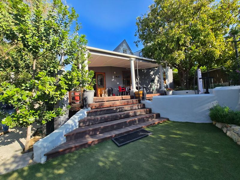Rear view of the property featuring a covered patio with timber decking, classical columns, and a landscaped garden area with artificial lawn.