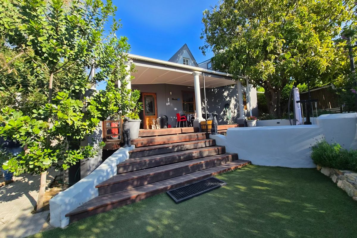 Rear view of the property featuring a covered patio with timber decking, classical columns, and a landscaped garden area with artificial lawn.