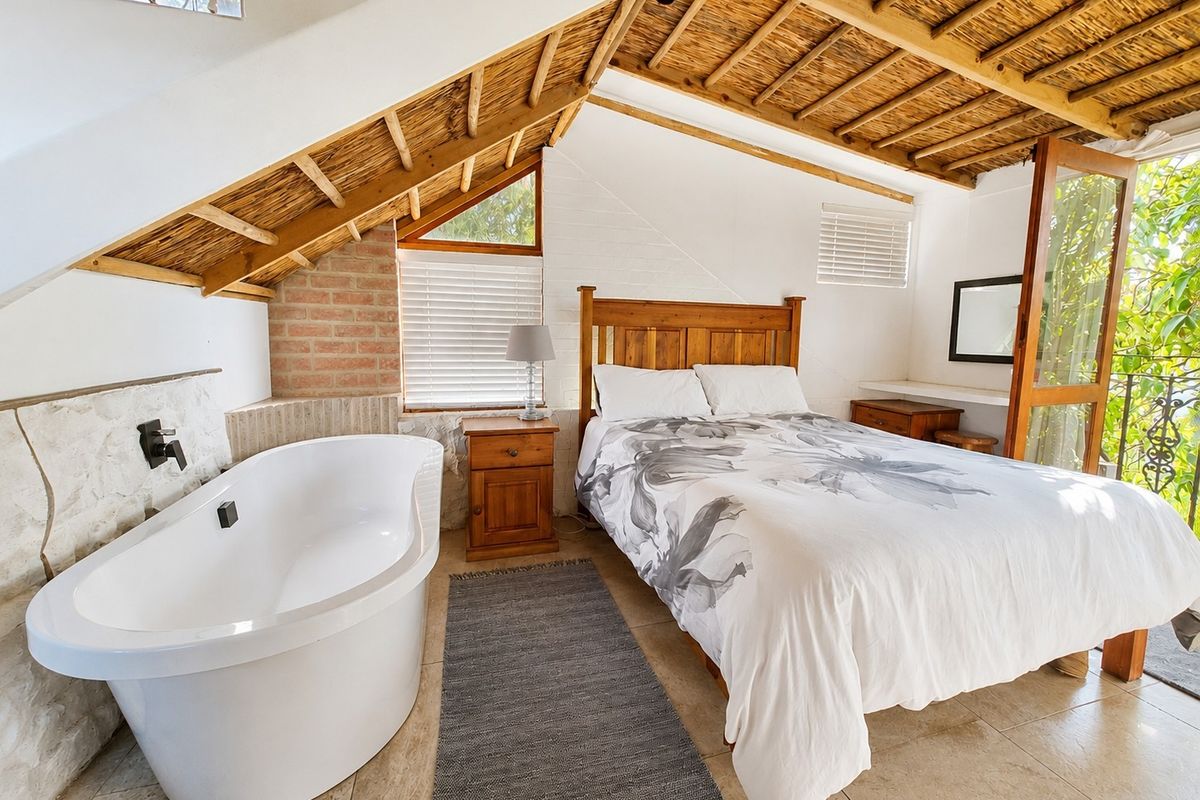Unique loft-style bedroom featuring an exposed thatch ceiling, stone wall accents, and an integrated freestanding bathtub, with direct access to an outdoor area.