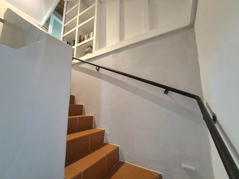 A bright staircase featuring terracotta-style floor tiles, a sleek black metal handrail, and integrated built-in shelving.