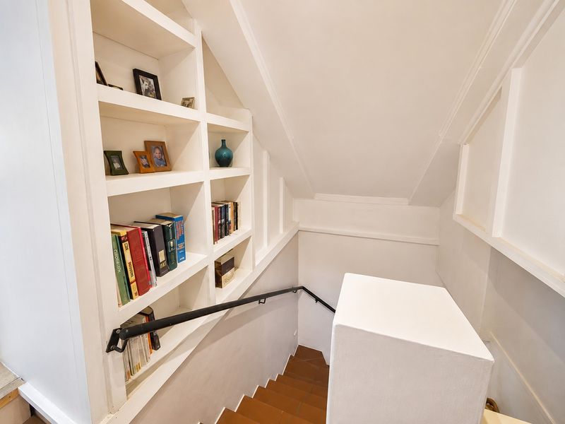 A well-maintained staircase featuring built-in shelving units and a modern black handrail, finished with clean white trim and tiled steps.