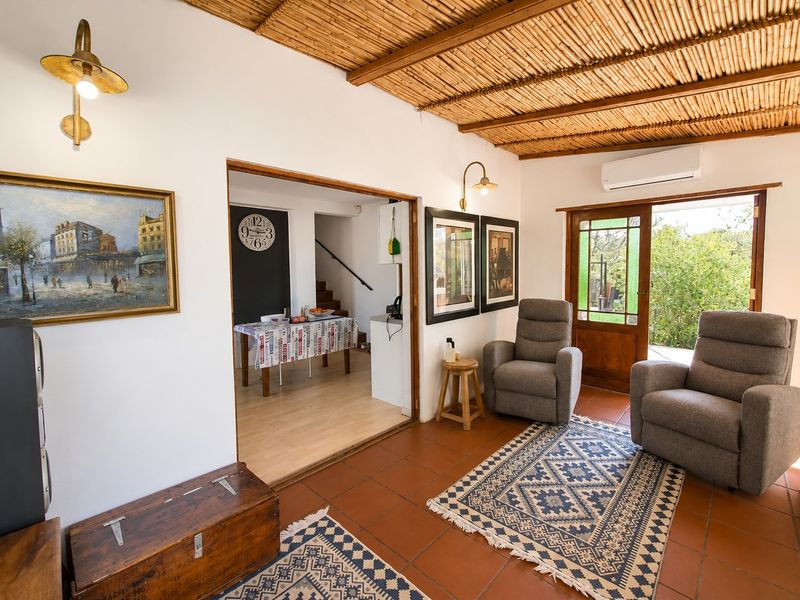 A cozy living room featuring a unique bamboo ceiling, terracotta floor tiles, and direct access to the outdoor area via a timber-framed glass door.